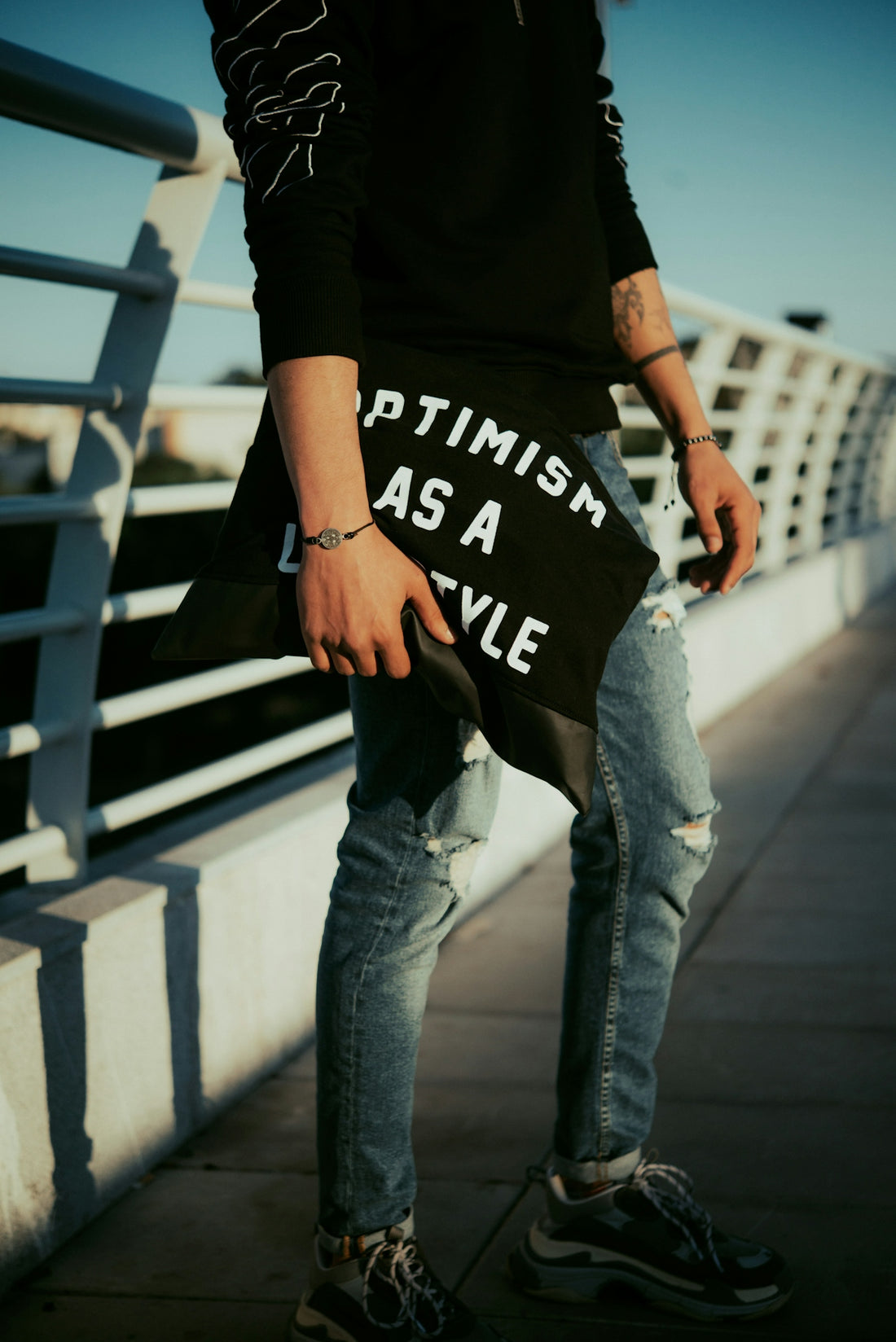 man in black t-shirt and blue denim jeans standing on bridge during daytime
