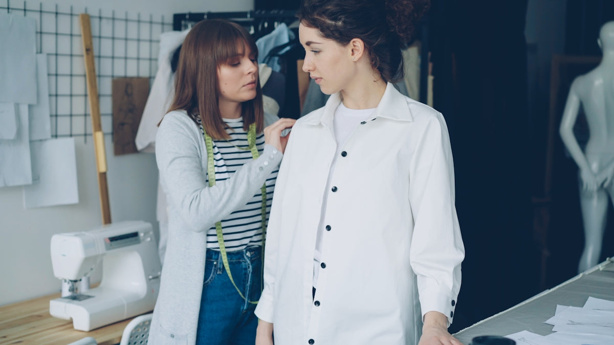 A seamstress adjusts a garment on a model.