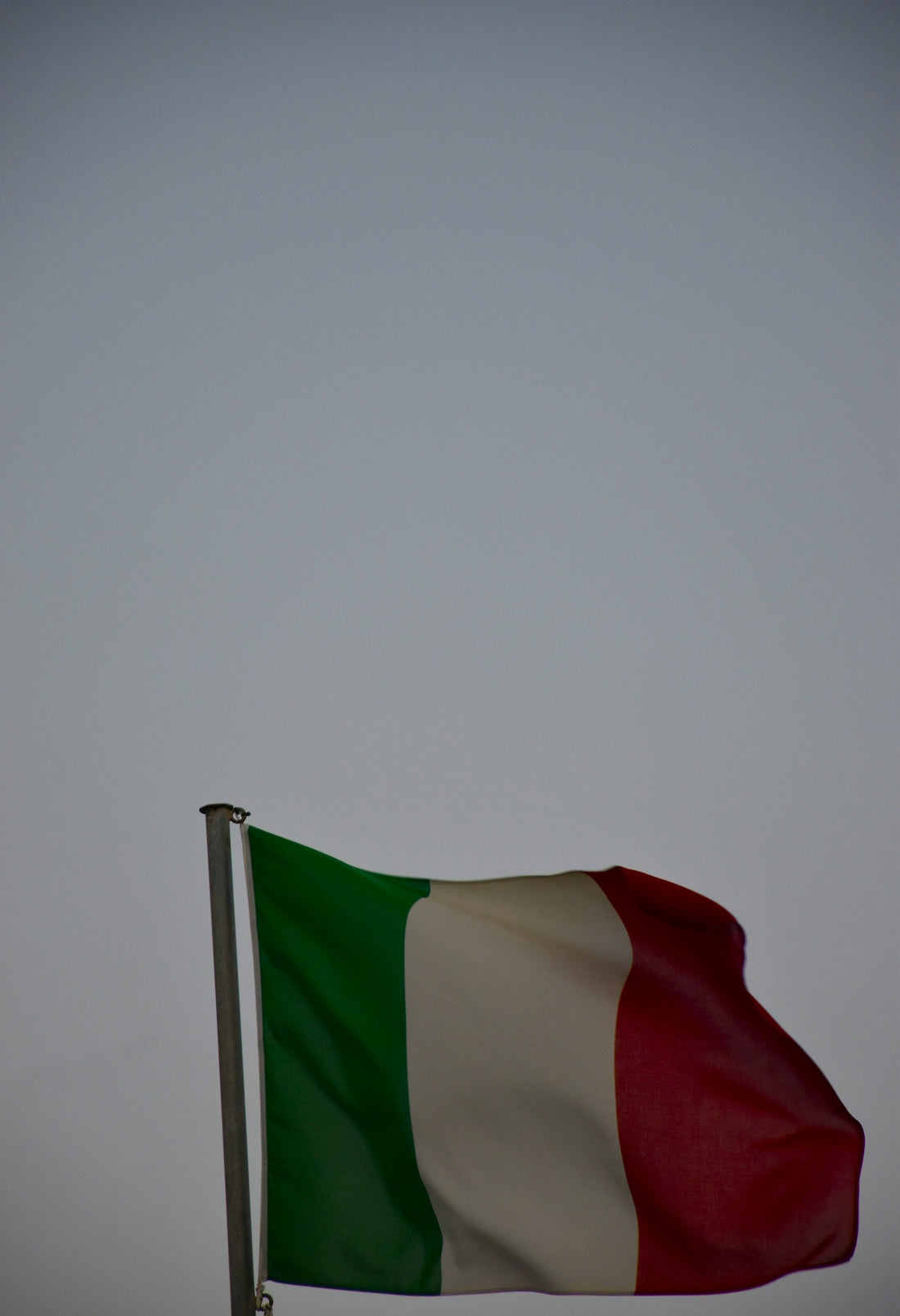 The italian flag waves against a grey sky.