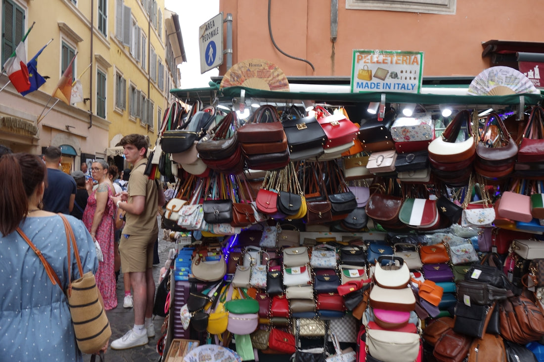 Street stall selling many leather handbags and accessories.